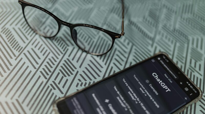 Eyeglasses next to a smartphone displaying the ChatGPT AI app on a patterned surface.