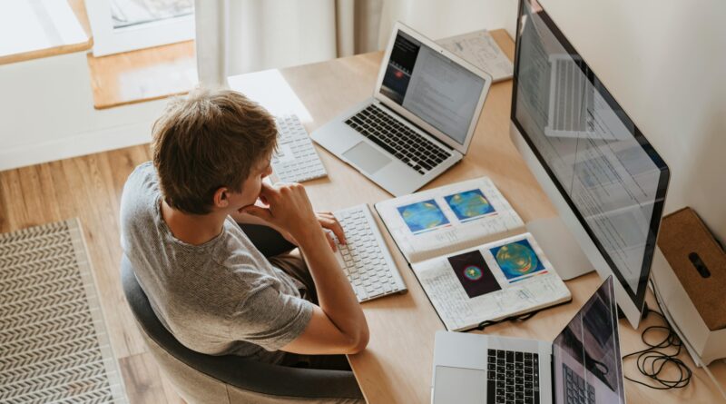 Top view of young programmer working on multiple laptops in a modern office setting.